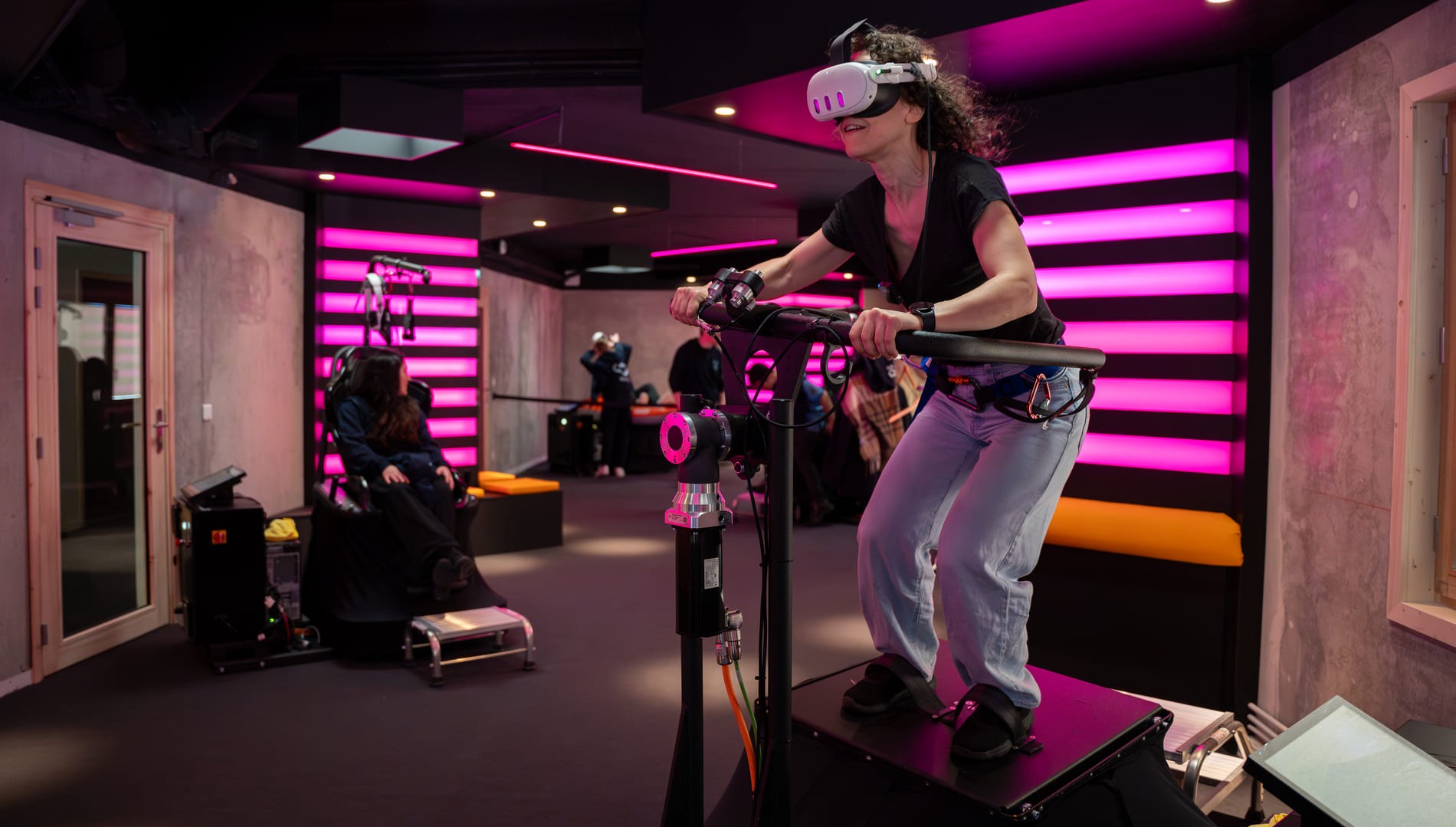 VR simulators room with a woman trying the MTB, and several other people in the background